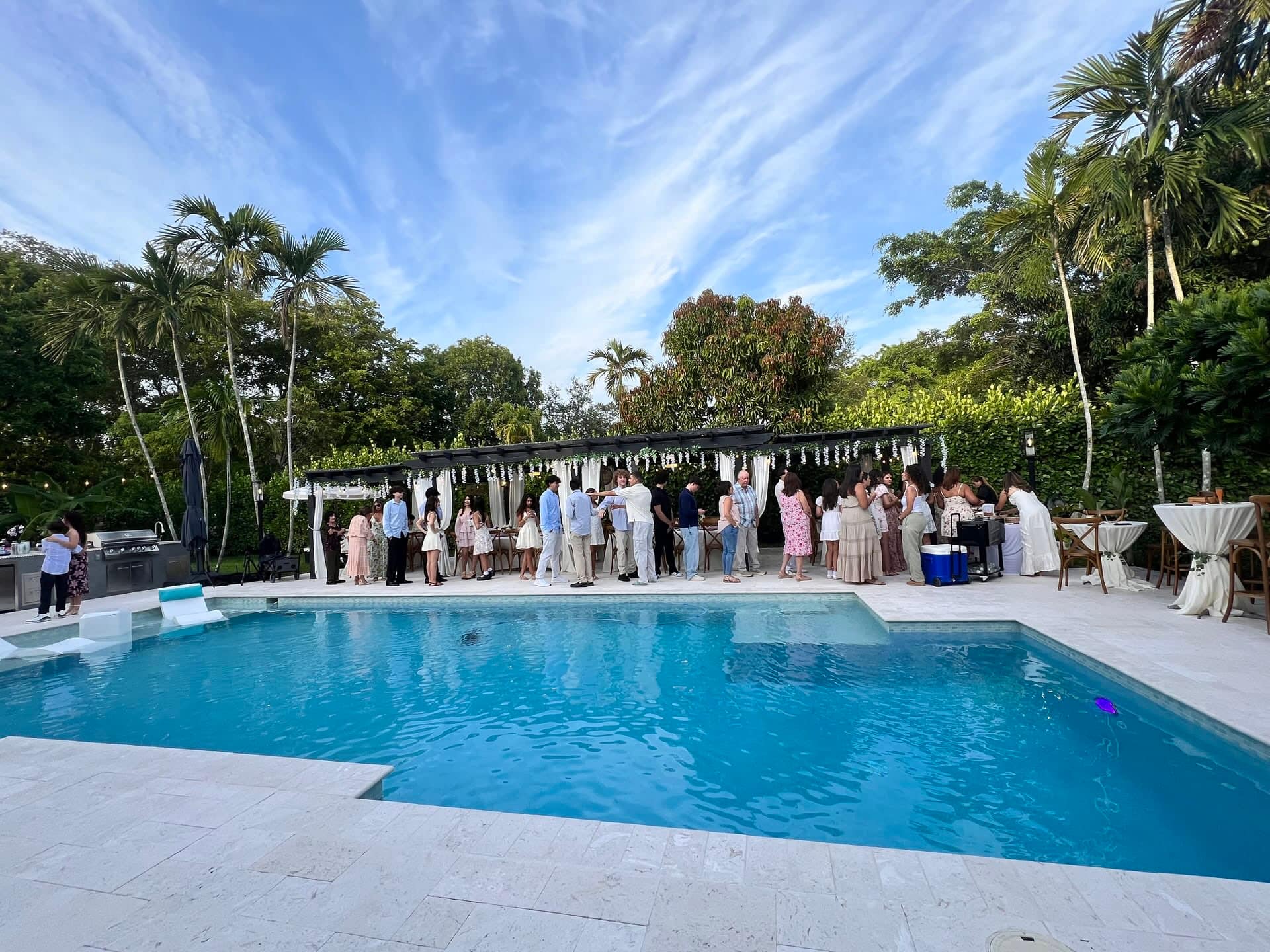 Miami backyard pool party at golden hour with pergola, cocktail bar, and guests gathered poolside